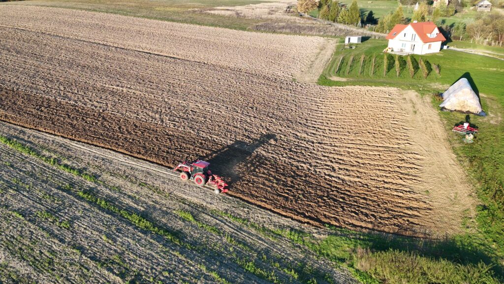 widok z lotu ptaka na traktor, który orze pole w pochyłym terenie